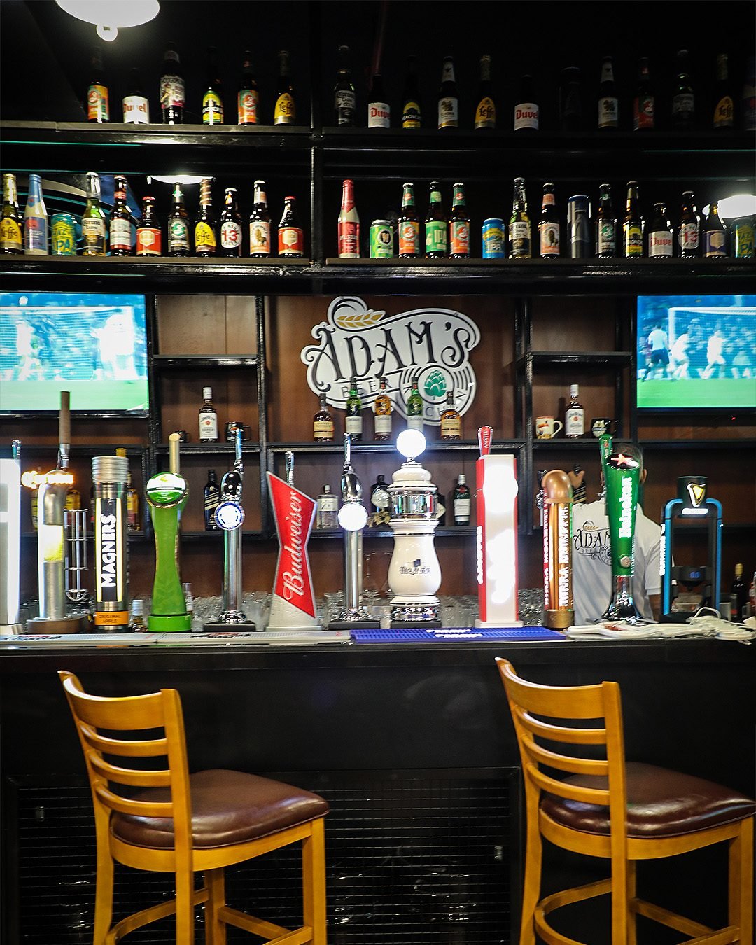 The bar at Adam's Beer Kitchen JVC — draught taps, bottle wall and the Adam's sign
